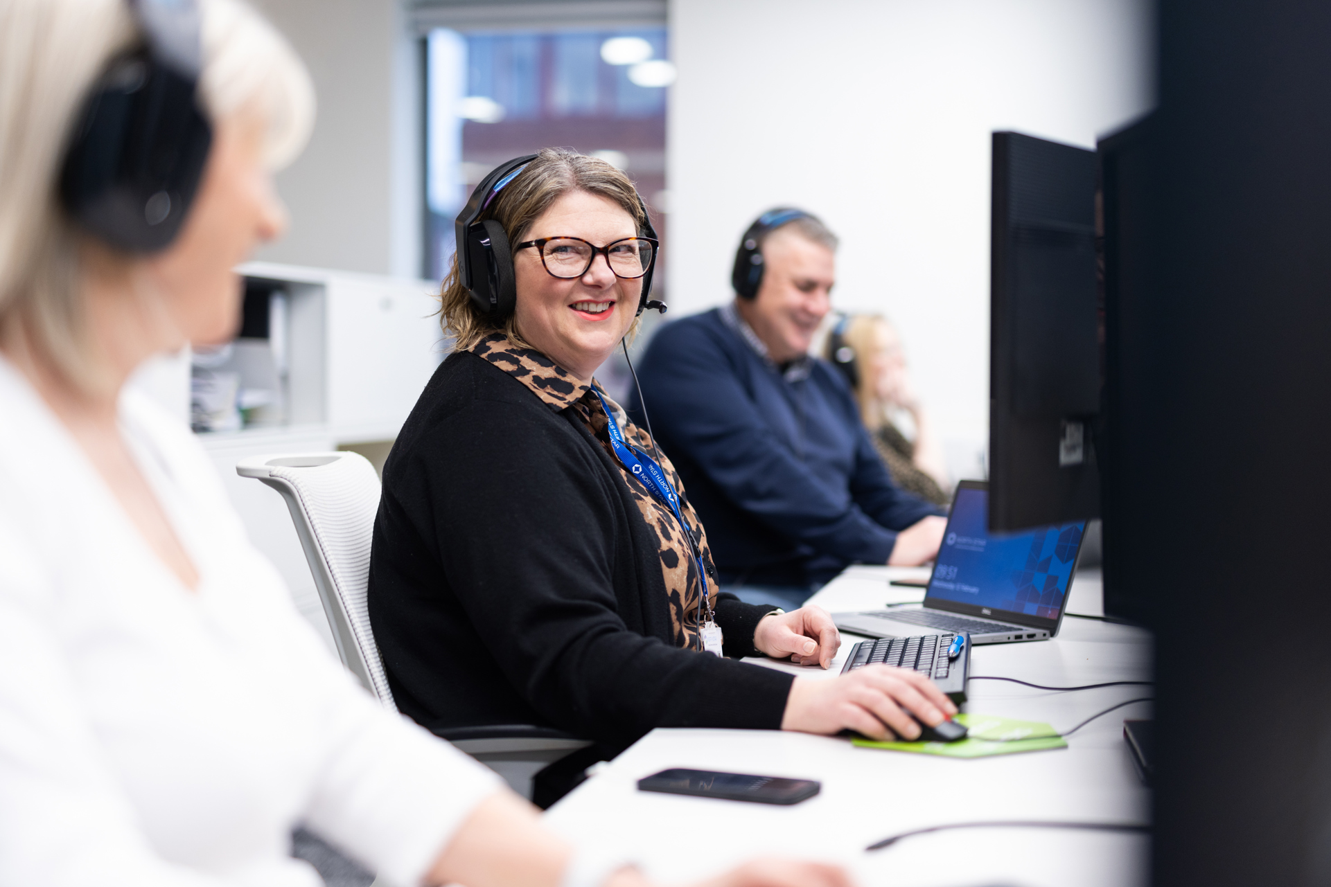 A woman sat at a desk in front of a computer smiling with a headset on.